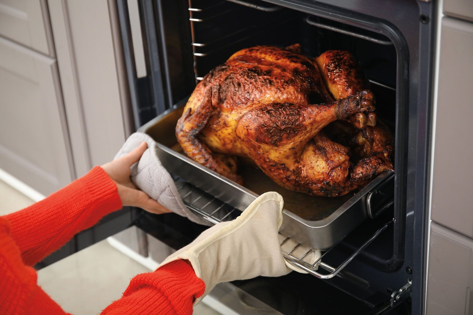 Woman,Taking,Tasty,Baked,Turkey,From,Oven,In,Kitchen.,Thanksgiving